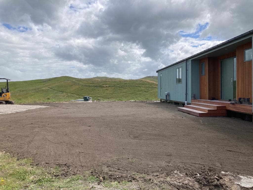 Rural site preparation with excavator and new build in background