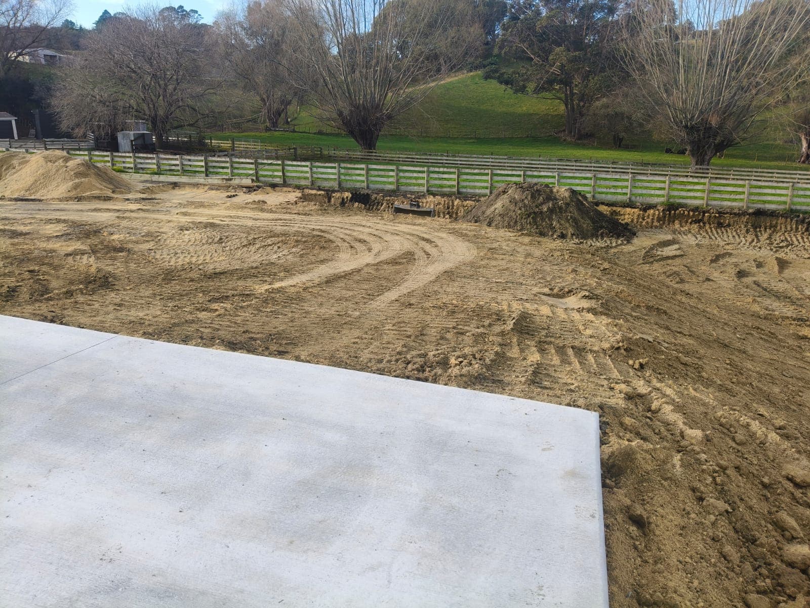 Concrete slab edge overlooking a large excavated earthworks site with tyre tracks