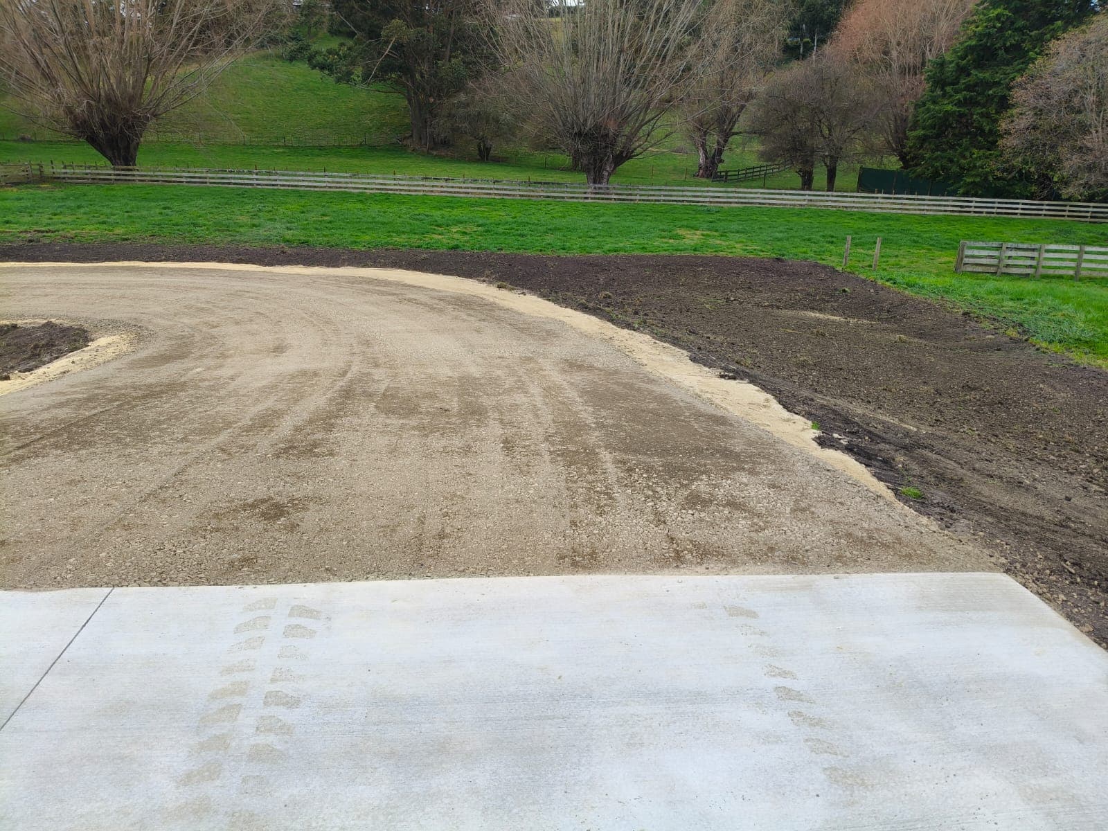 Completed concrete pad meeting a graded gravel driveway curving through a green paddock