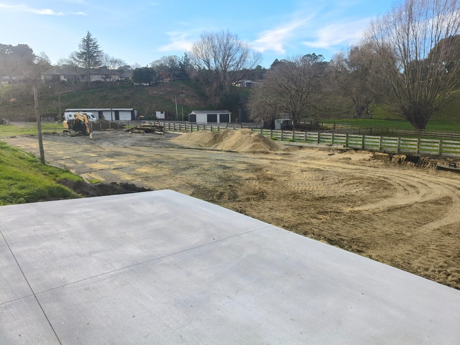 Freshly poured concrete slab with excavator and sand piles on rural property