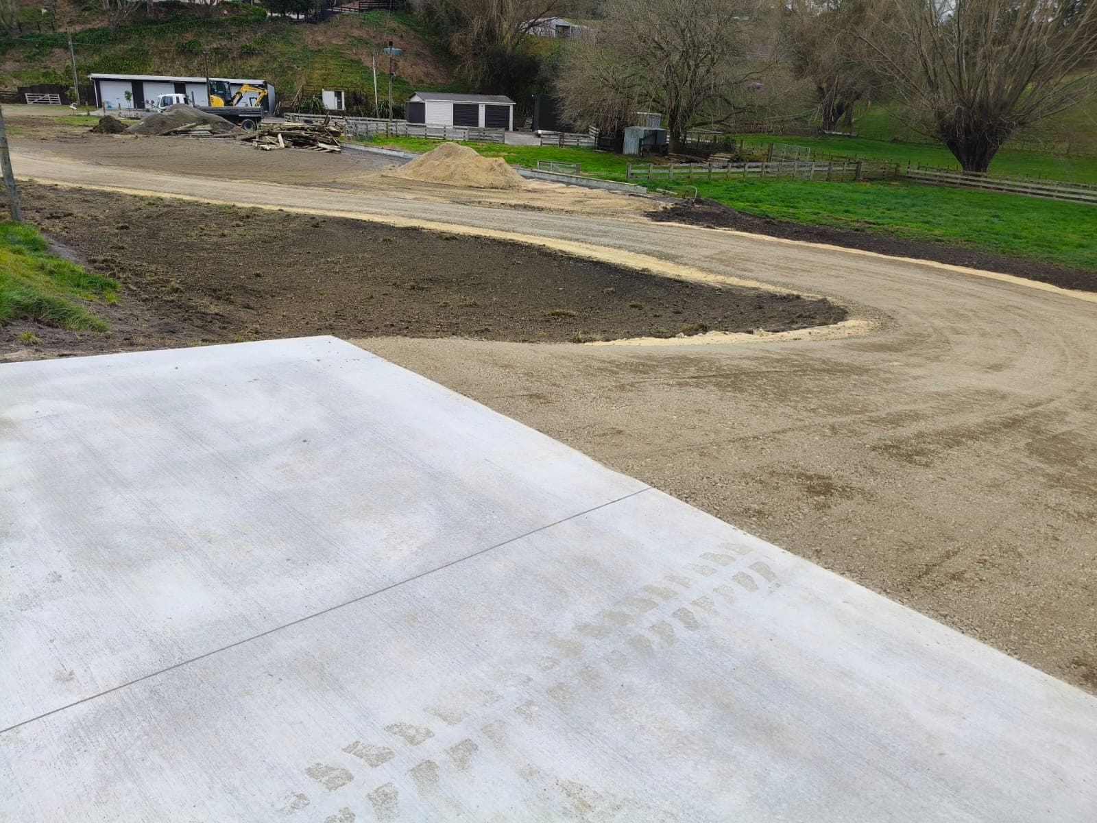 Elevated view of finished concrete pad and curved gravel driveway looping around fresh topsoil