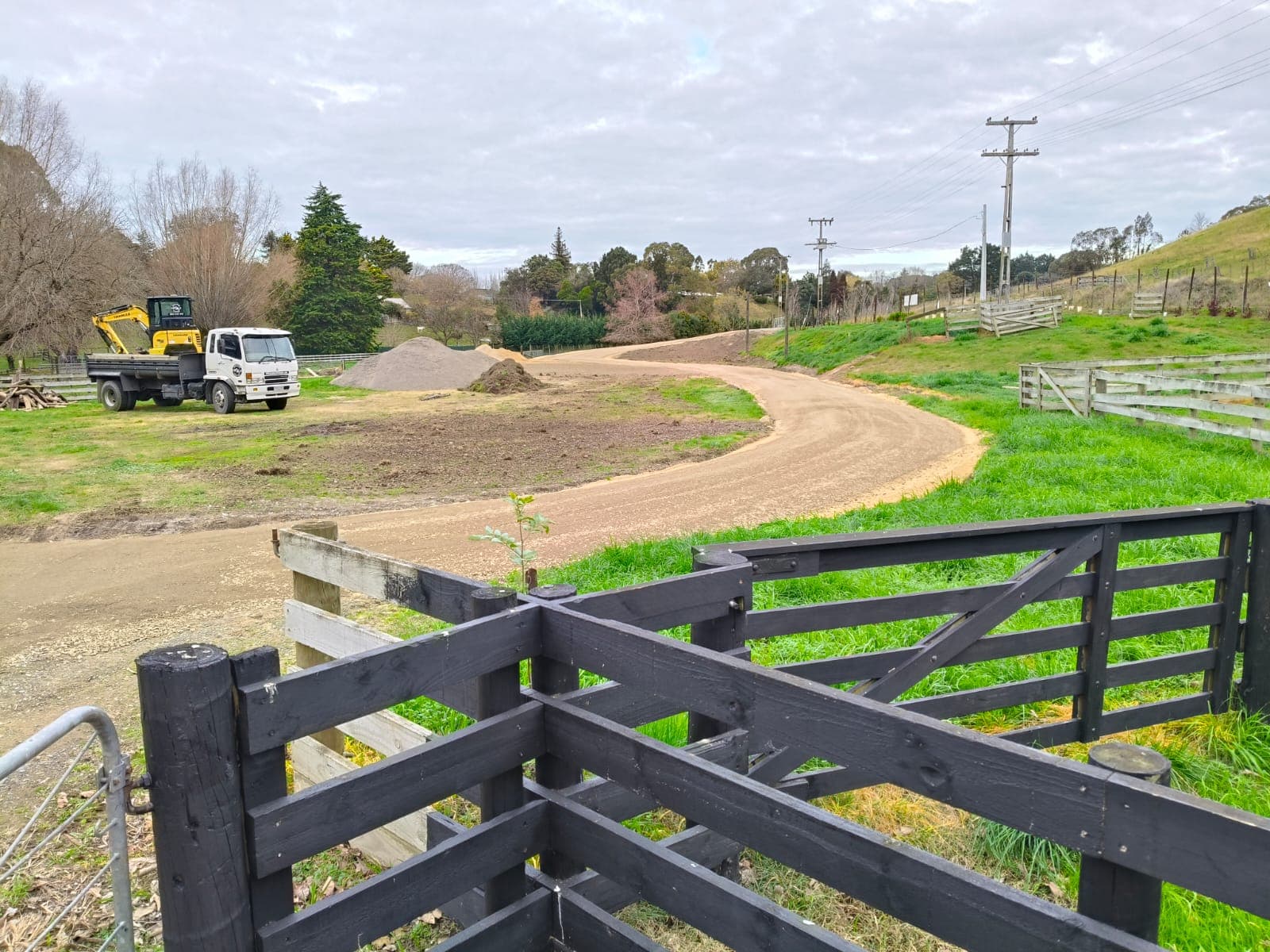 View through a black farm gate to the completed curved gravel driveway