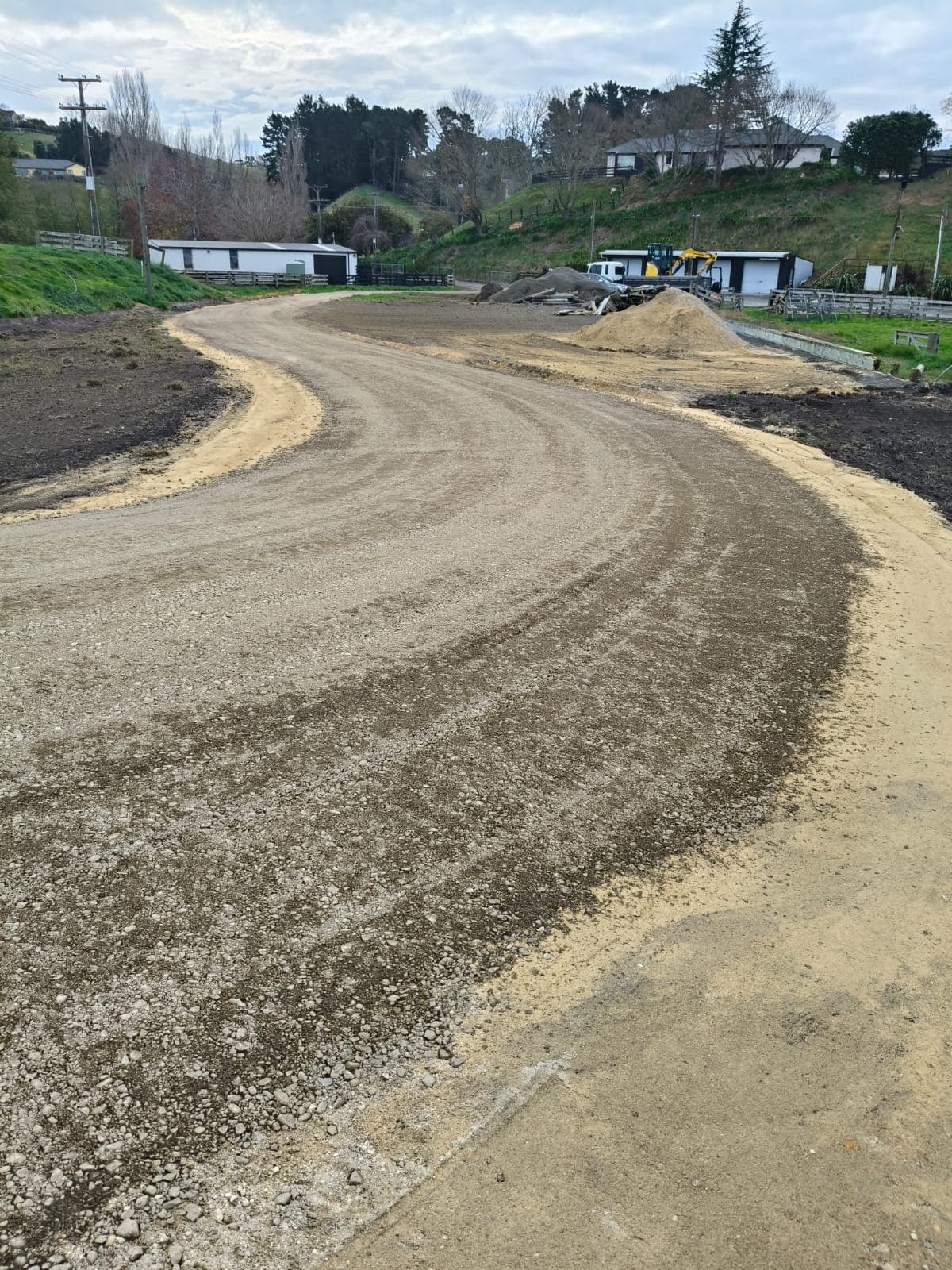 Wide curving gravel driveway leading toward farm buildings