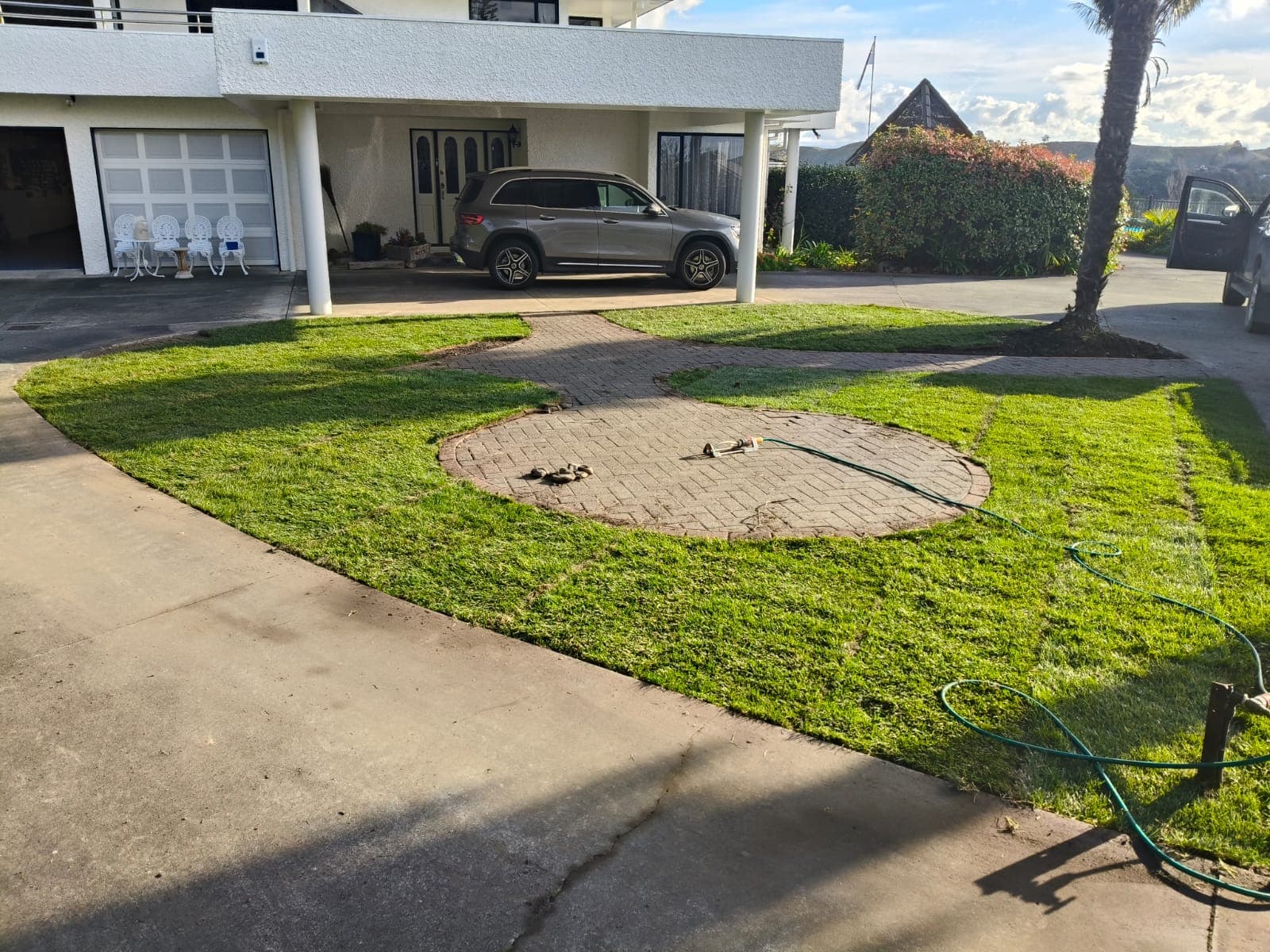 Completed lush green instant lawn around the circular paver feature in front of the house