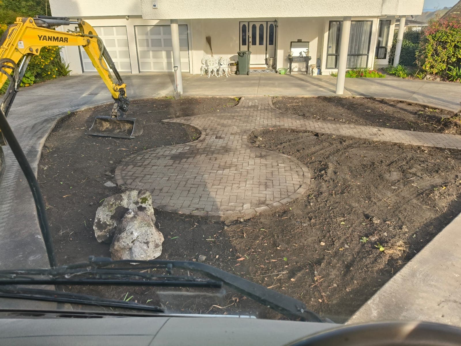 Excavator clearing the old garden with bare soil beds around brick paver paths before turf was laid