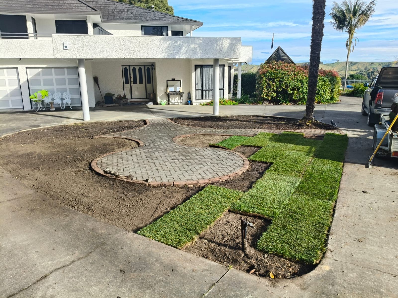 Prepared and levelled ground with the first rolls of ready lawn being laid beside the paver path