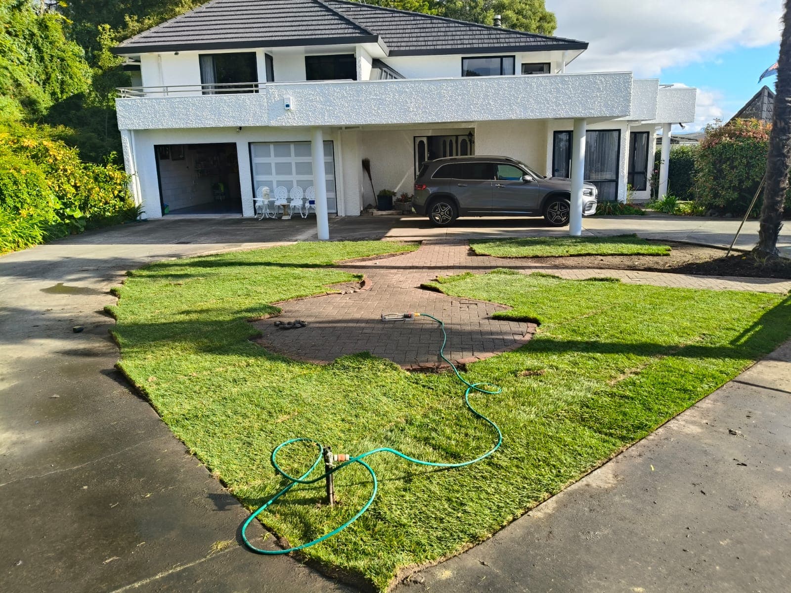 Front garden mid-installation with turf partially laid and watering in progress