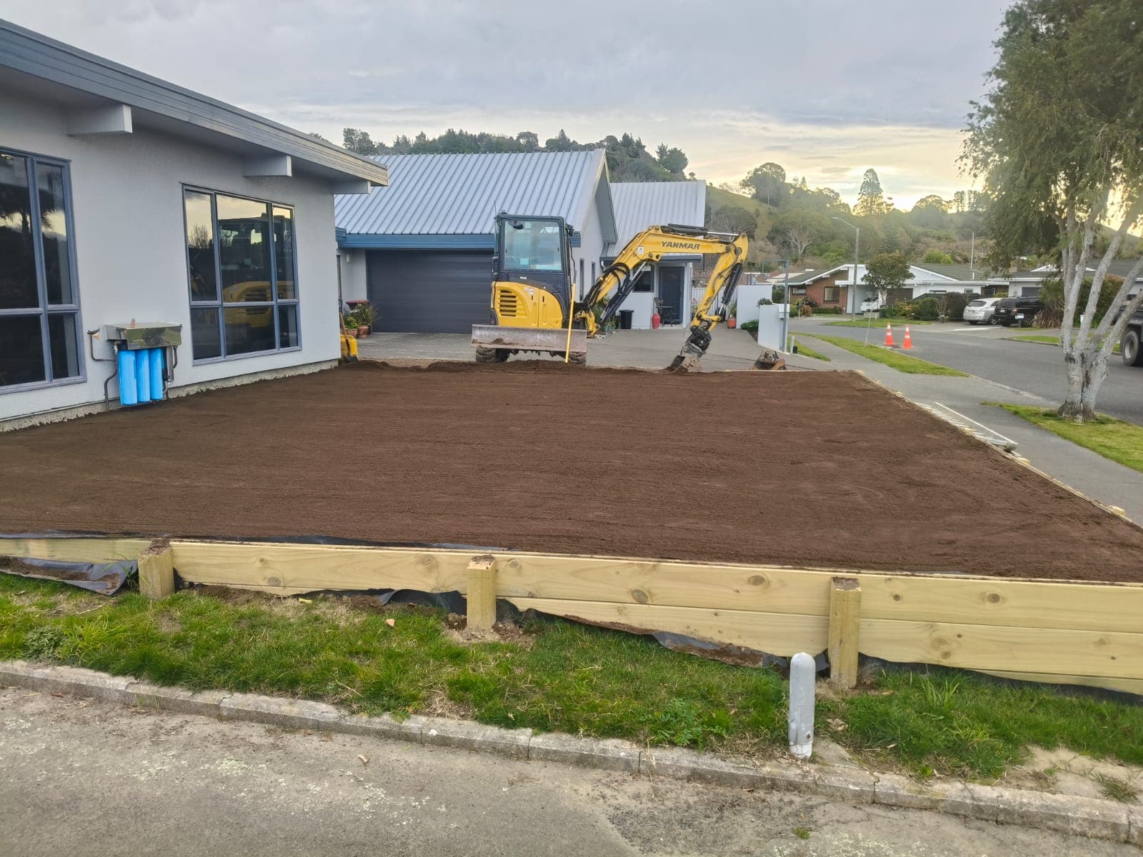 Prepared front section with levelled topsoil, timber retaining wall and excavator by the street