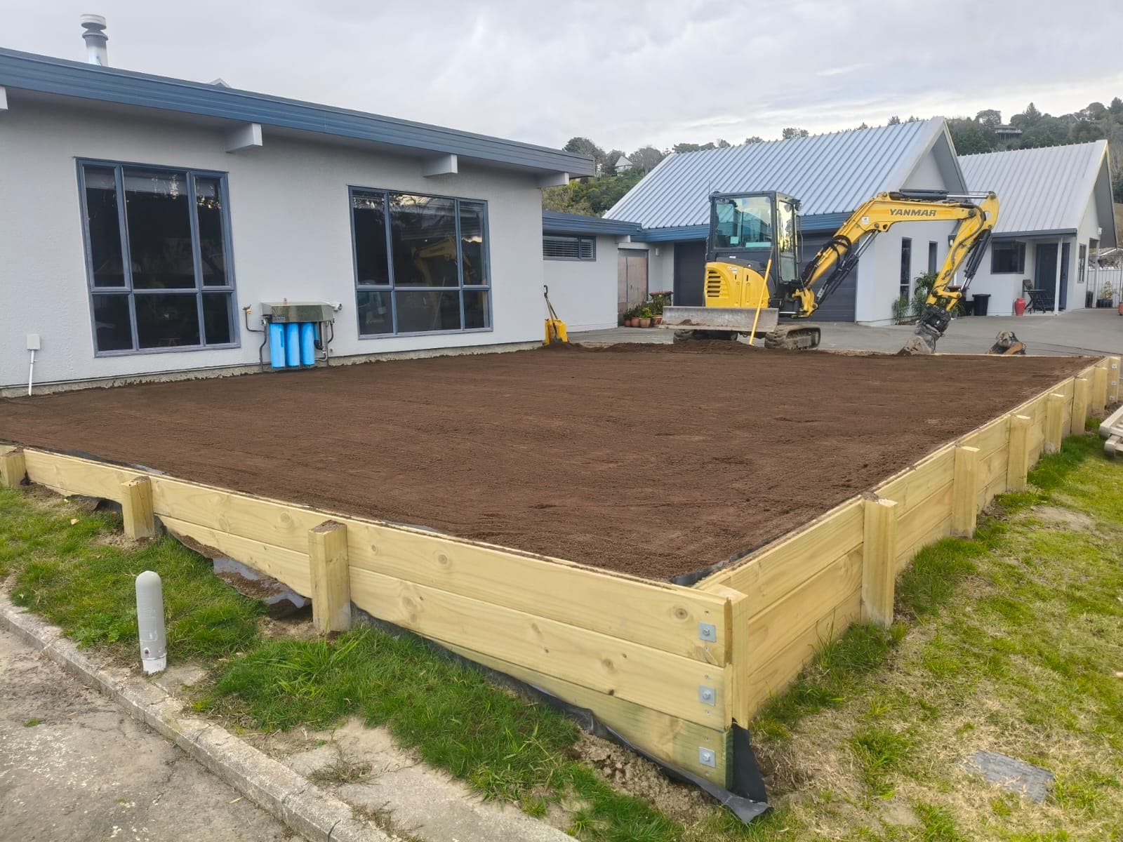Freshly levelled topsoil bed framed by timber retaining wall beside a modern home