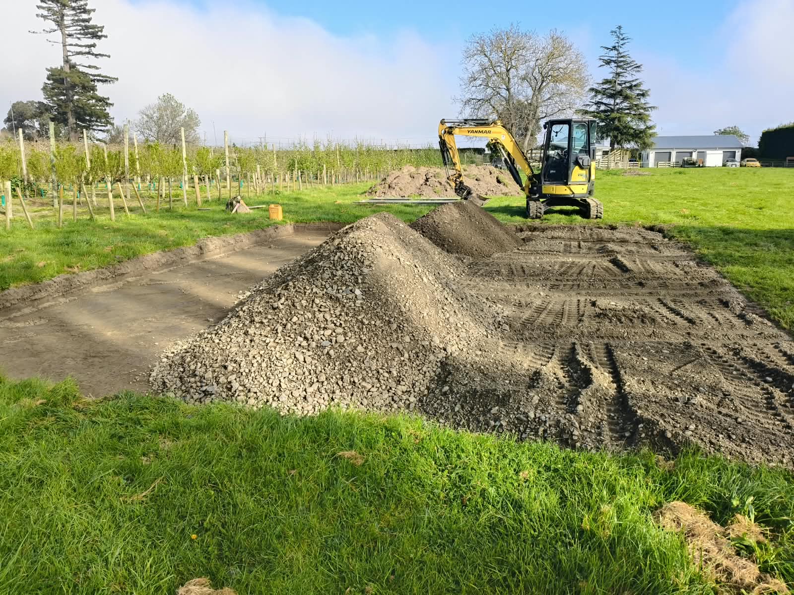 Excavator working beside a foundation excavation with aggregate stockpiled nearby