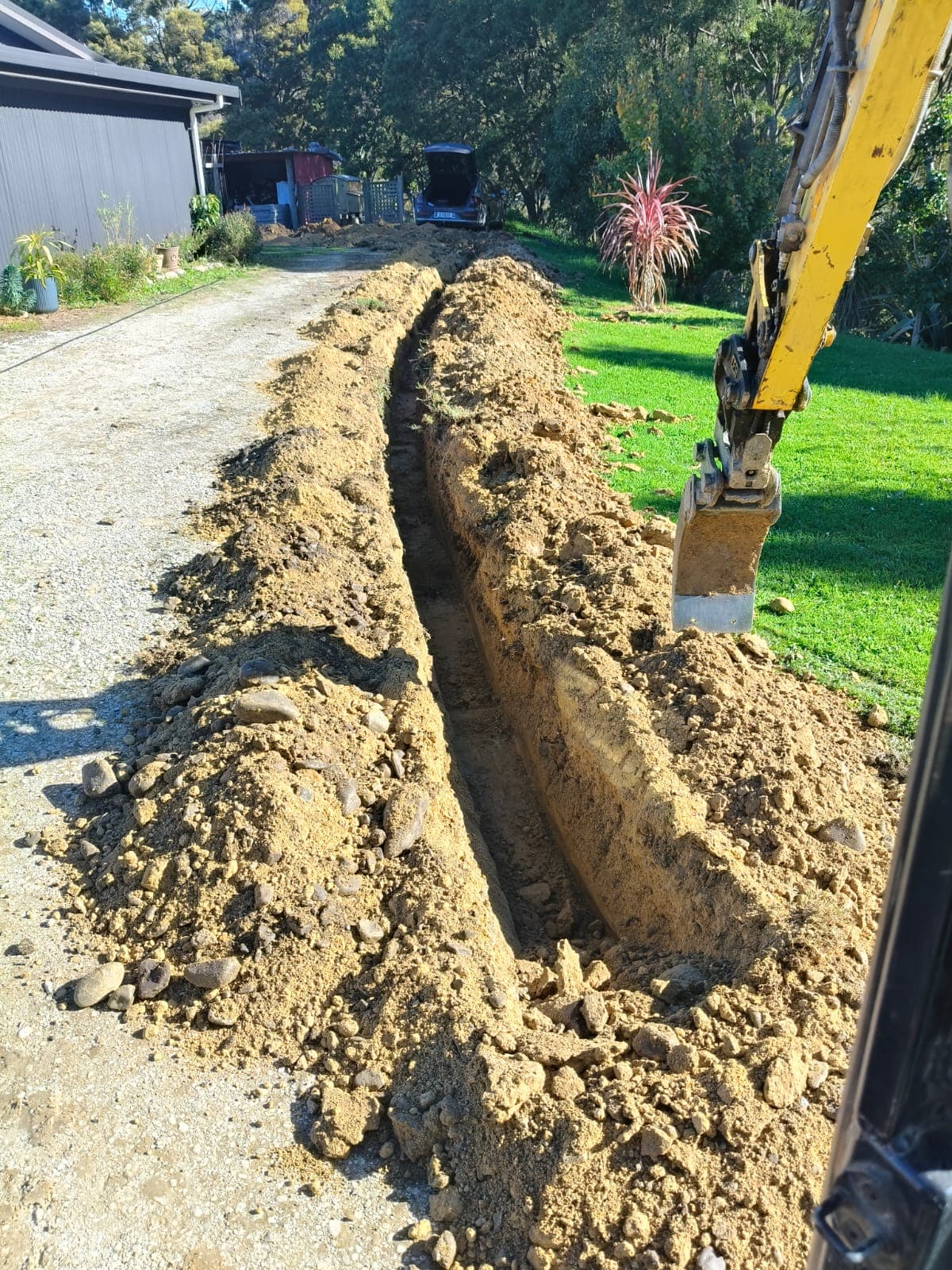 Long service trench dug along driveway with excavator bucket visible