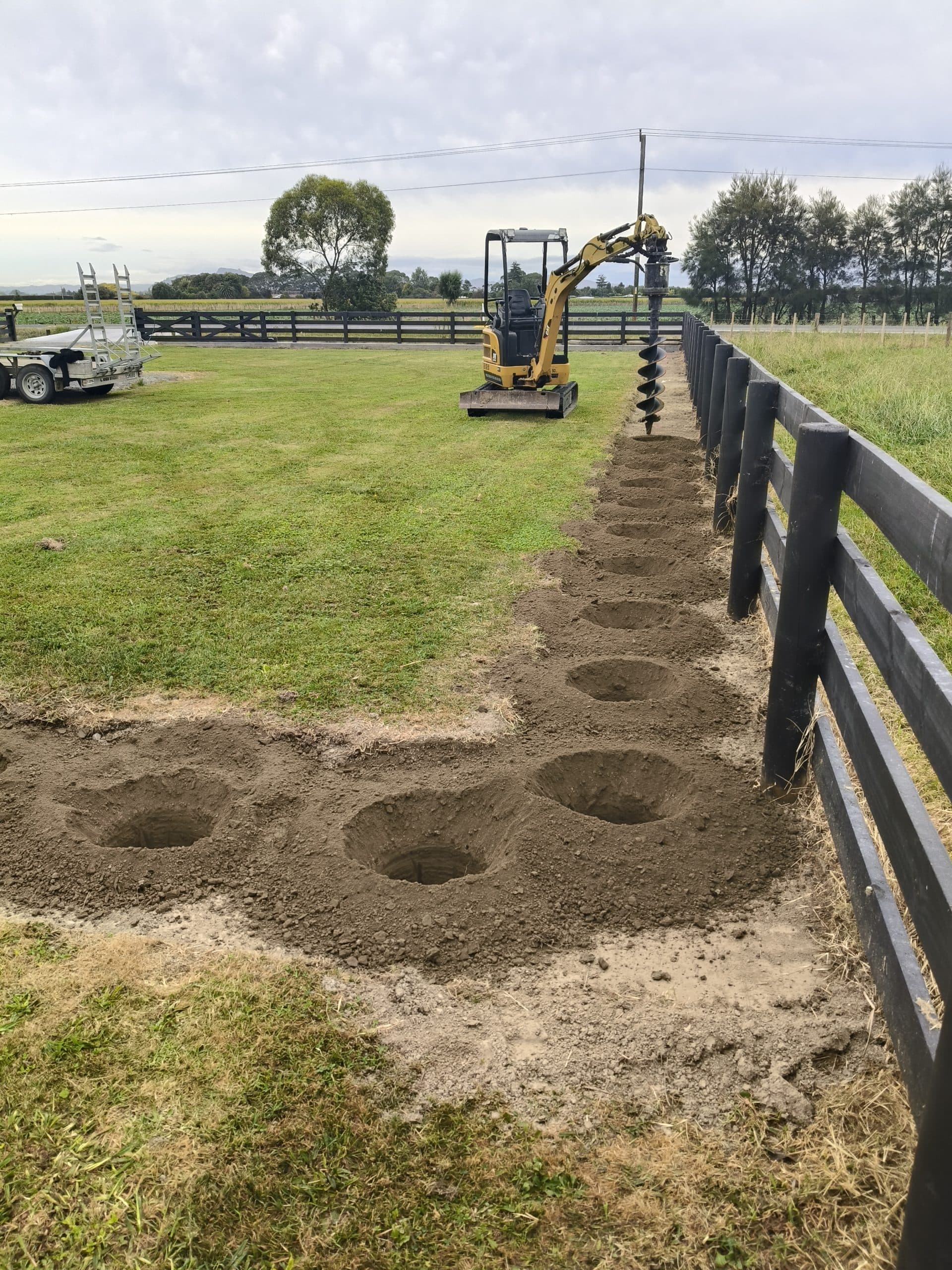 CAT mini excavator with auger attachment drilling fence post holes