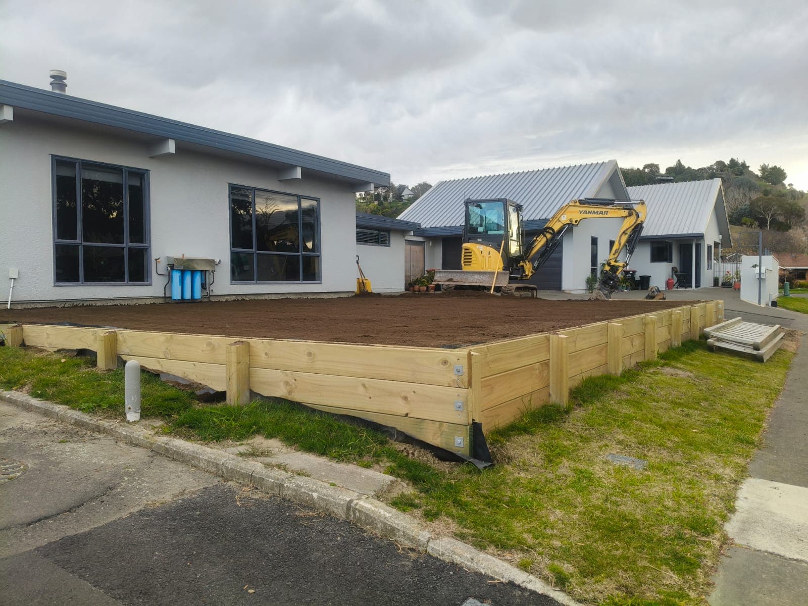 Levelled topsoil section bordered by a new timber retaining wall with a Yanmar excavator on site
